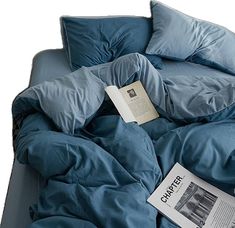 an open book is laying on top of a blue comforter with pillows and sheets