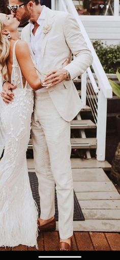 a man in a white suit and woman in a white dress kissing on the cheek