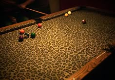 an animal print pool table with eight balls on it and two people in the background