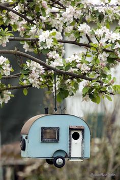 an old blue camper is hanging from a tree with white flowers in the background