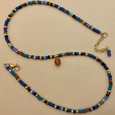 a beaded necklace with blue, red and gold beads on a white table top