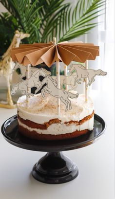 a cake with an umbrella on top of it sitting on a black plate next to a potted plant