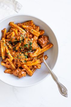 a white bowl filled with pasta covered in sauce and parsley next to a fork