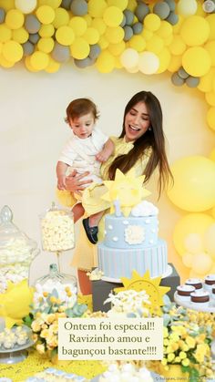 a woman holding a baby in front of a cake