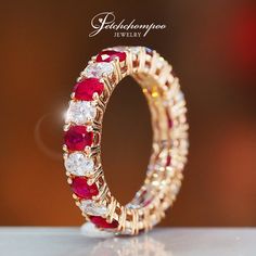 a gold ring with red and white stones on it's side, sitting on top of a table