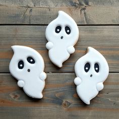 three decorated cookies with black eyes and white ghost faces on top of a wooden table