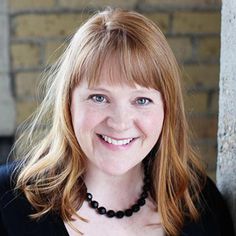 a woman with red hair and blue eyes smiles at the camera while leaning against a brick wall