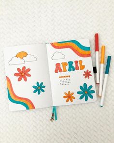 an open notebook with colorful flowers and the word april written on it next to two markers