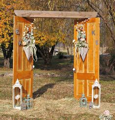 two wooden doors are decorated with flowers and candles in front of some trees on the grass