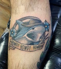 a tattoo on the leg of a man with a shark and ribbon