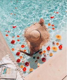 a woman in a straw hat sitting on the edge of a pool surrounded by flowers