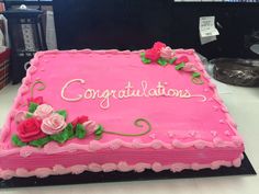 a pink cake with roses and congratulations written on the top is sitting on a table