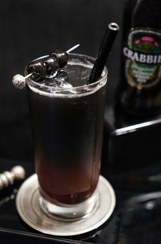 an alcoholic drink is sitting on a table next to a bottle and tongs in it