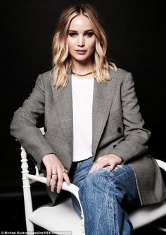 a woman sitting on top of a white chair in front of a black background wearing jeans and a blazer