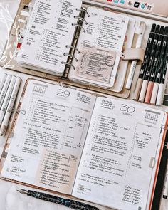 an open planner with pens and pencils in it on a marble counter top next to other items