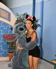 a woman in a black bathing suit hugging a gray stuffed animal with a red bow on her head