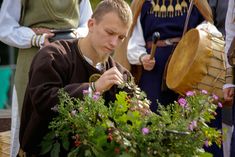 a man is looking at some flowers in front of other men with instruments and drums