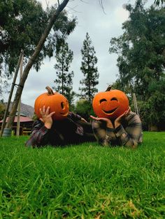 two people laying in the grass with pumpkins on their heads and one person holding an orange pumpkin