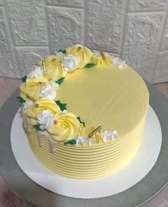 a cake with yellow frosting and white flowers on the top is sitting on a platter