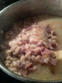 a pot filled with soup and meat on top of a stove next to a wooden spoon