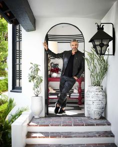 a man is standing on the steps in front of a doorway with potted plants