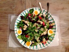 a salad with hard boiled eggs and greens in a bowl on top of a wooden table