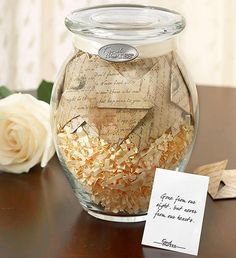 a glass jar filled with lots of paper on top of a table next to a white rose