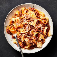 a white plate topped with pasta covered in sauce and meat next to a fork on top of a table