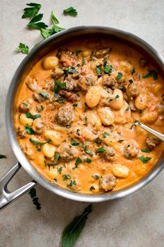 a pot filled with pasta and meatballs on top of a white counter next to parsley