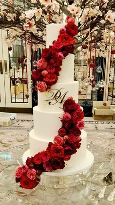 a three tiered white wedding cake with red flowers on the side and monogrammed initials