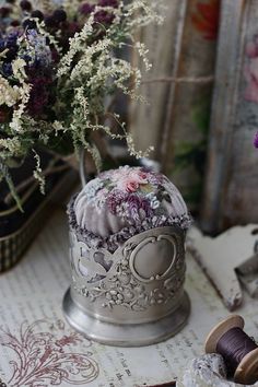 a vase with flowers in it sitting on a table next to some sewing thread and spools