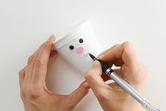 a person is holding a cup with a cat face on it and writing on the side