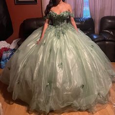 a woman in a green ball gown is standing on the floor next to a couch