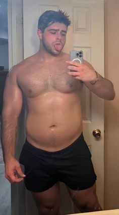 a shirtless man taking a selfie in front of a mirror with his cell phone