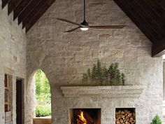 a living room with a fire place next to a stone wall and ceiling fan above it