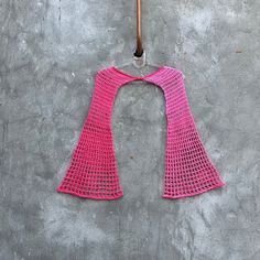 a pink crocheted top hanging on a clothes hanger with an umbrella in the background