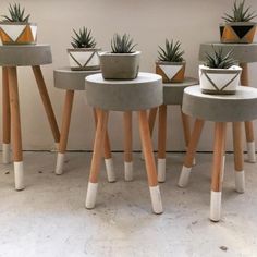 four cement planters sitting on wooden legs with succulents growing out of them