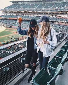 two young women standing on the bleachers at a baseball game holding up drinks