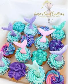 cupcakes decorated with blue, pink and purple icing are in a box