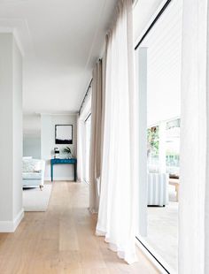 an image of a room with white curtains on the windowsills and wood flooring