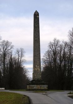 an obelisk stands in the middle of a road surrounded by trees and grass