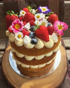 a cake with strawberries, blueberries, and flowers on top sitting on a plate