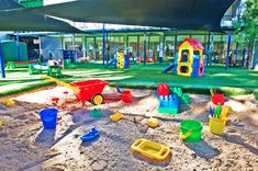 An outdoor sheltered childcare sandpit playground with a grassy area on the other side. Many equipment and toys throughout the playground. School Readiness, Shopping Centre, Shopping Center