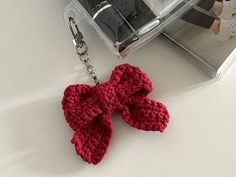 a red knitted bow keychain sitting on top of a white table next to a pair of shoes