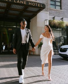 a man and woman holding hands while walking down the street in front of a hotel