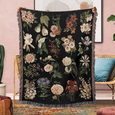 a black blanket with flowers on it in front of a chair and potted plant