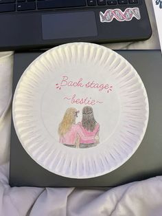 a paper plate with two women sitting on top of it next to a laptop computer