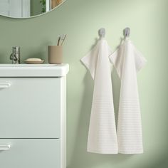 two white towels hanging from hooks on a green wall