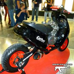 a black and red motorcycle on display in a room with people looking at the bikes