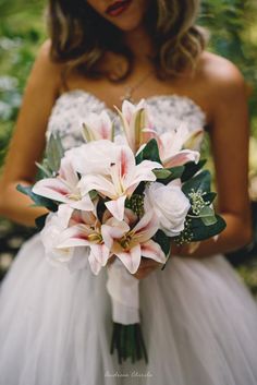 a woman in a wedding dress holding a bridal bouquet with white lilies and greenery